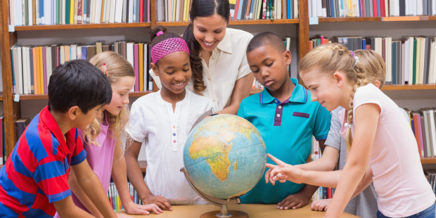 Multi ethnic children and teacher looking at globe in the library