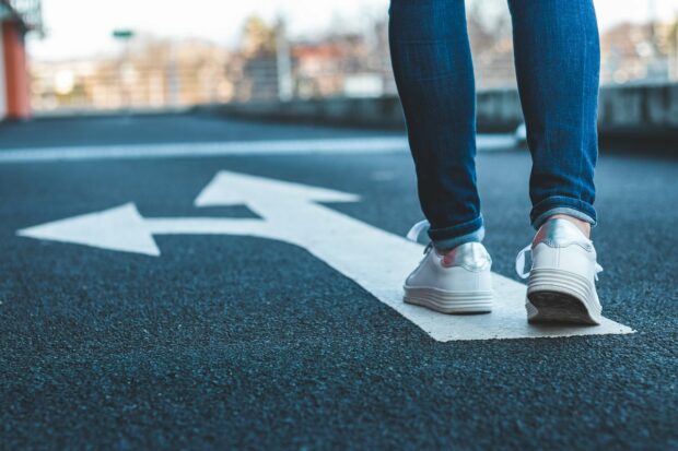 Legs in jeans with trainers standing on an arrow that goes in two directions