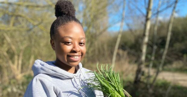 Black woman holding plants in forest setting